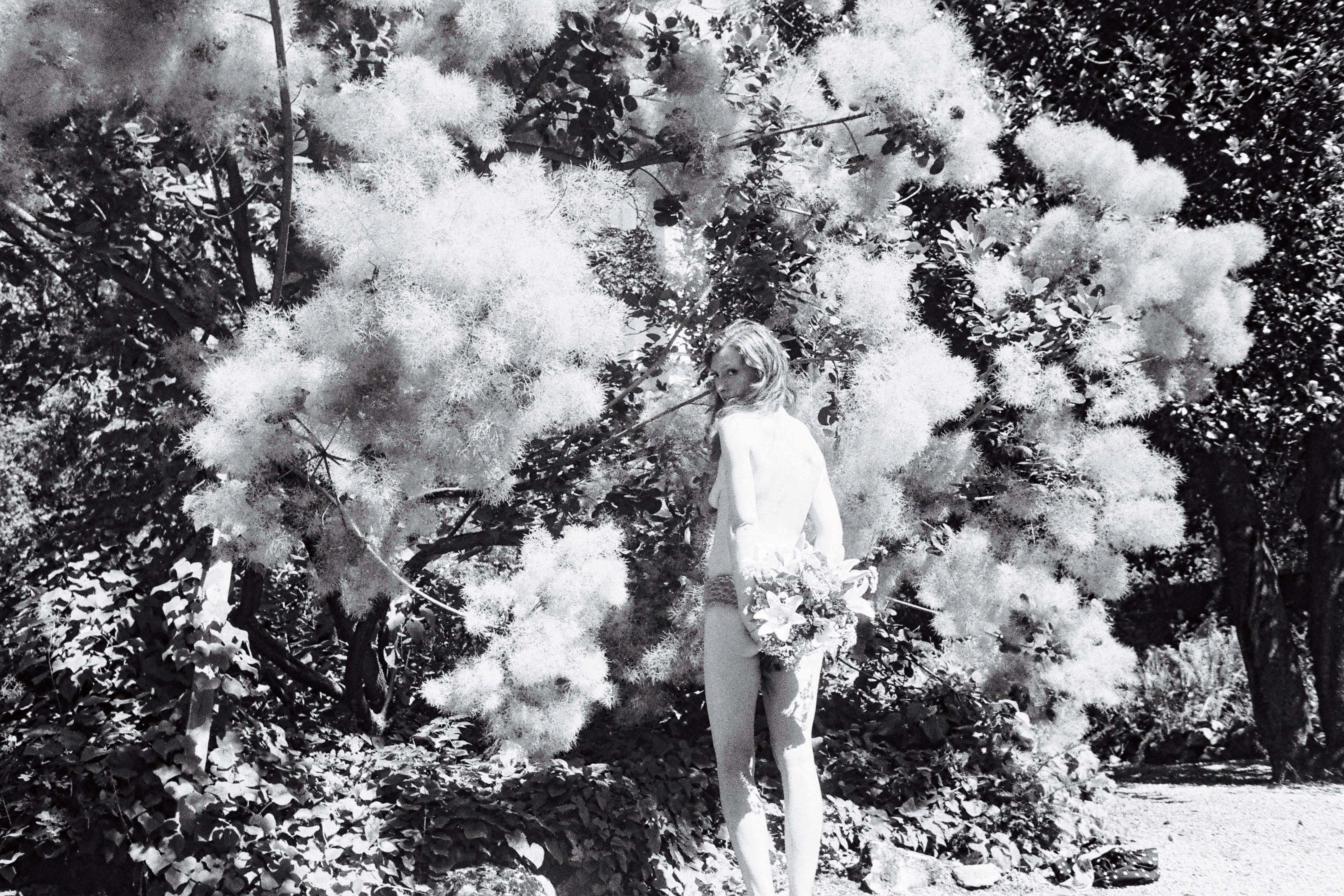Jeune femme prise en photo de dos, devant un mur de fleurs, noir et blanc, par Marianne Maric